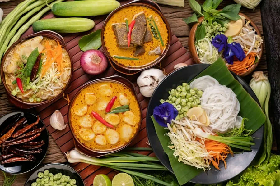 สำรับอาหารไทยในถ้วยไม้และจานใบตอง มีขนมจีน แกง และผักเคียง